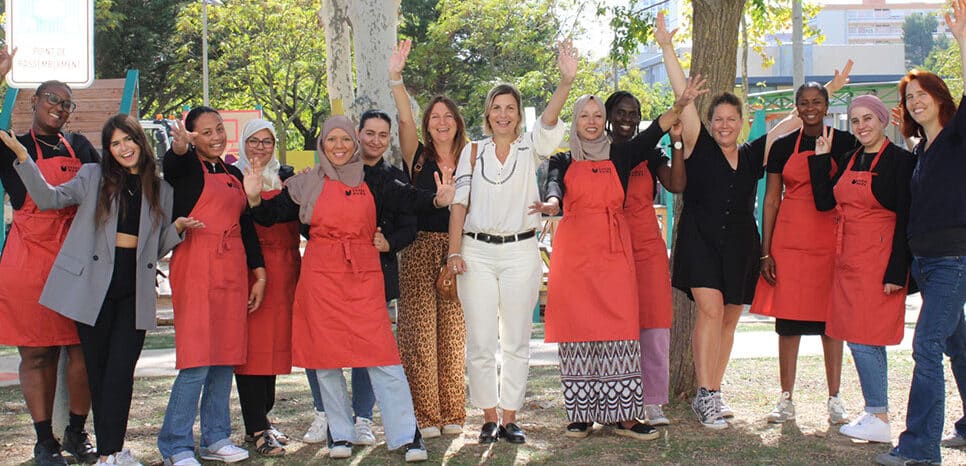 Un groupe de femmes entrepreneures en tabliers rouges célèbrent ensemble en plein air, bras levés et sourires complices, lors d'un temps d'accompagnement collectif organisé par France Active en Occitanie.
